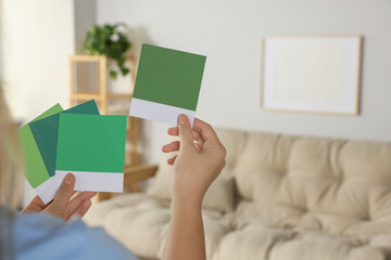 Woman with color sample cards choosing paint shade for wall in room, closeup. Interior design