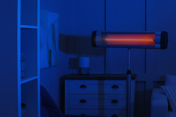 Electric infrared heater in dark living room at night