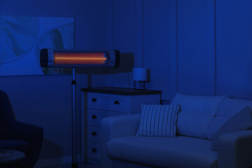 Electric infrared heater in dark living room at night