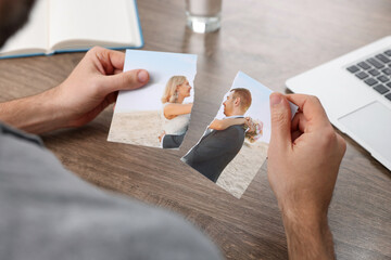 Man holding parts of photo at table indoors, closeup. Divorce concept - obrazy, fototapety, plakaty