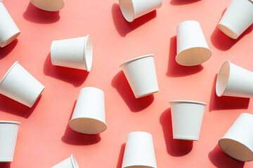 Several disposable white paper cups. Mock up to go coffee cups with shadows on pink.
