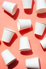 Several disposable white paper cups. Mock up to go coffee cups with shadows on pink.
