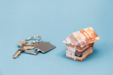 Key and house keychain on real estate with origami from russian rubles. Light blue background. Copy space. Concept of mortgage and leasing of real estate