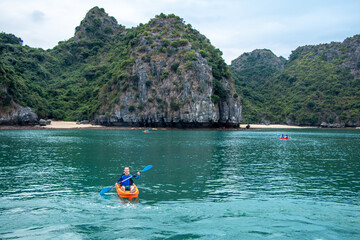 Kayaker on the water in front of a limestone karst island with rainforest and sandy beaches in the Ha Long Bay UNESCO World Heritage site in Qiang Ninh Province in northern Vietnam