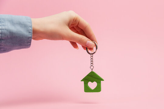 Female hand holding a house keychain. Pink background. Concept of mortgage, leasing of real estate