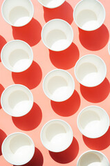 Several disposable white paper cups. Mock up to go coffee cups with shadows on pink.