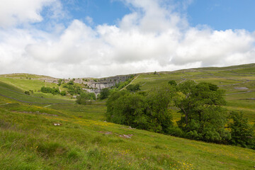 Fototapeta na wymiar Far view of Malham Cove, with meadows and limestone moorland beyond, Yorkshire Dales National Park, North Yorkshire, UK