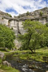 The sheer 80-metre (260 foot) high cliff face of the famous Malham Cove, with the Malham Beck flowing away from its foot, North Yorkshire, UK