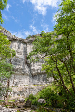 The sheer 80-metre (260 foot) high cliff face of the famous Malham Cove, with the Malham Beck flowing away from its foot, North Yorkshire, UK
