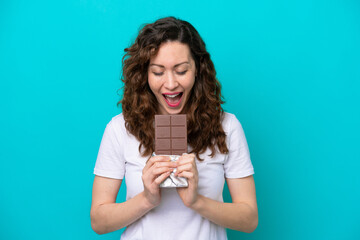 Young caucasian woman isolated on blue background eating a chocolate tablet