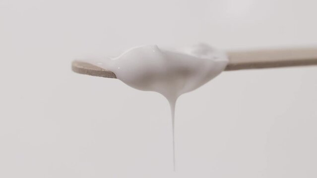 White cosmetic liquid cream texture on a wooden spatula close-up. Beauty background with dripping body product.