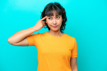 Young Argentinian woman isolated on blue background making the gesture of madness putting finger on...