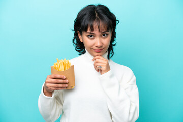 Young Argentinian woman holding fried chips isolated on blue background thinking