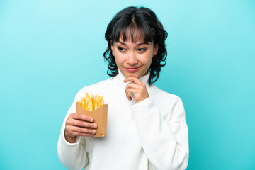 Young Argentinian woman holding fried chips isolated on blue background looking to the side and smiling