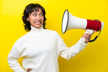 Young Argentinian woman isolated on yellow background holding a megaphone with stressed expression