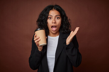Young business woman drinking a take-away coffee surprised and shocked.