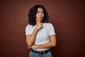 Young colombian curly hair woman isolated on brown background looking sideways with doubtful and...
