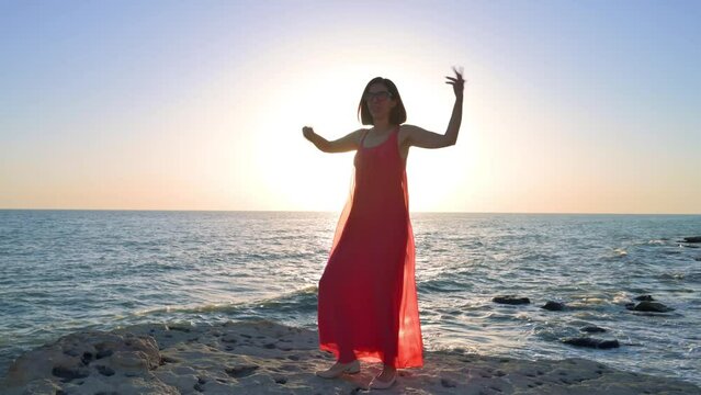 Happy woman in red dress dancing near the Baltic sea on a sunset. Woman impressed with the nature. 4k footage UHD 3840x2160 