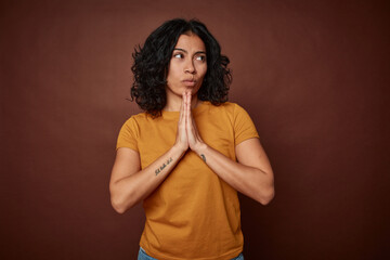 Young colombian curly hair woman isolated on brown background praying, showing devotion, religious...