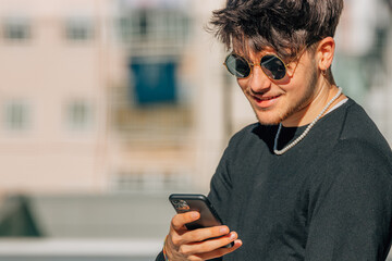 Fototapeta premium young man with sunglasses looking at mobile phone in the street