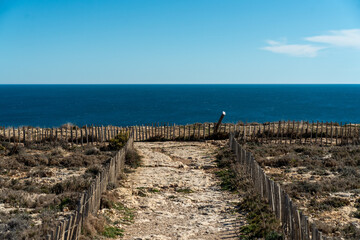 Fototapeta na wymiar Off the beaten paths destination. Stone walking path along the edge above the sea without people on a sunny day.
