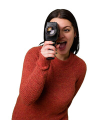 A young woman happily films with an antique video camera on an isolated background. She captures...