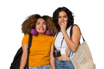 Two diverse friends on a beach vacation with vintage camera, beach bag, and travel pillow biting fingernails, nervous and very anxious.
