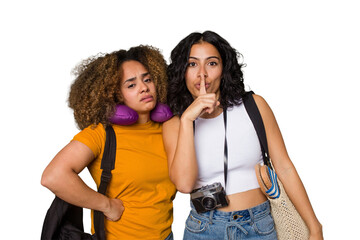 Two diverse friends on a beach vacation with vintage camera, beach bag, and travel pillow keeping a secret or asking for silence.