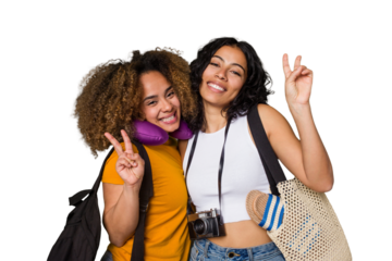 Two diverse friends on a beach vacation with vintage camera, beach bag, and travel pillow joyful and carefree showing a peace symbol with fingers.