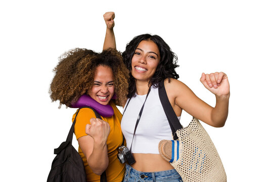Two diverse friends on a beach vacation with vintage camera, beach bag, and travel pillow raising fist after a victory, winner concept.