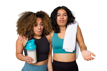 Two best friends are ready to go to the gym, one of them holds a protein shake, shrugs shoulders and open eyes confused.