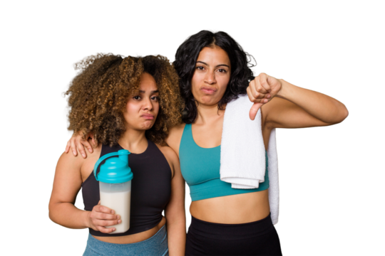 Two best friends are ready to go to the gym, one of them holds a protein shake, showing a dislike gesture, thumbs down. Disagreement concept.