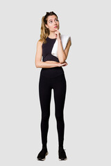 Fototapeta premium Full body of young woman in sportswear, fit and athletic, embodying a healthy and active lifestylelooking sideways with doubtful and skeptical expression.