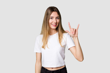 Young blonde posing for a portrait isolated, exuding natural beauty and radiance showing a horns gesture as a revolution concept.