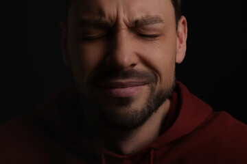 Fototapeta premium Sad man crying on black background, closeup