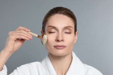 Woman massaging her face with jade roller on grey background