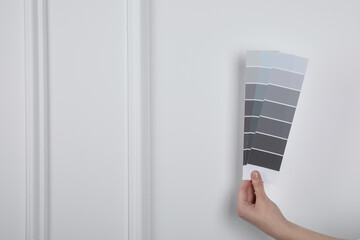 Woman with paint chips choosing color near white wall, closeup. Interior design