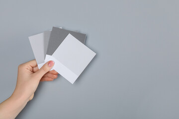 Woman with color sample cards choosing paint shade near grey wall, closeup. Interior design