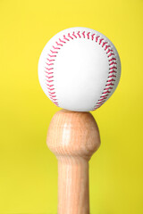 White ball on wooden baseball bat against yellow background, closeup. Sports equipment
