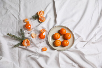Delicious fresh ripe tangerines and glasses on white bedsheet, flat lay