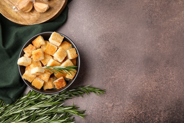 Delicious crispy croutons in bowl and rosemary on dark table, flat lay. Space for text