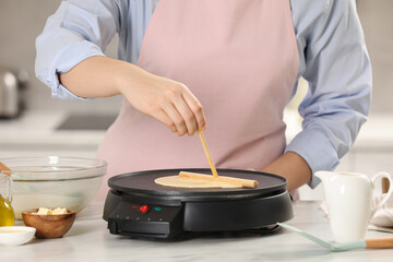 Fototapeta na wymiar Woman cooking delicious crepe on electric pancake maker at white marble table in kitchen, closeup