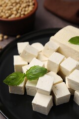 Delicious tofu cheese, basil and soybeans on brown table, closeup