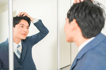 鏡の前でヘアセットをする若いサラリーマンの男性