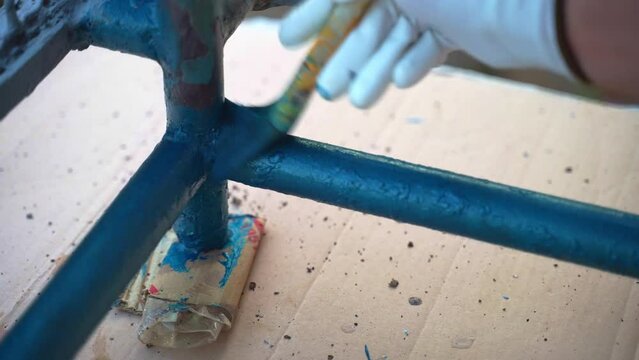 Renovation of aged corroded balcony frames with special modern chemical solutions, person hand in protective gloves using paintbrush for coating metal surface with blue colour, workman repairing steel