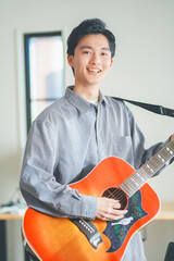 自宅でアコースティックギターを弾く若い男性