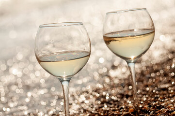 Two glasses of wine on the seashore in the waves and sparkling bokeh from water and pebbles