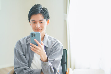 ソファに座ってスマートフォンを操作する若い男性
