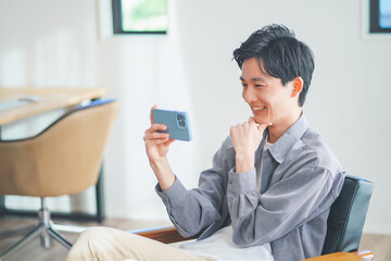 ソファに座ってスマートフォンで動画を見る若い男性