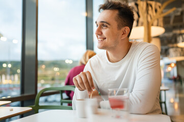 One man young adult Caucasian man sit at cafe or restaurant alone looking to the side having a cup of coffee real people copy space happy smile